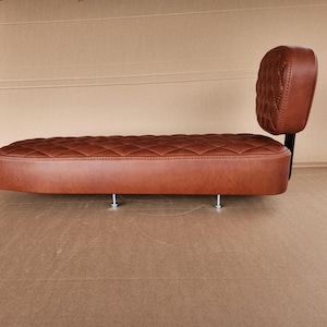 May include: A brown leather motorcycle seat with a diamond-stitched pattern. The seat has a backrest with a similar quilted design. The seat is mounted on a black metal frame with silver bolts.