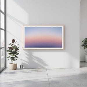 May include: A framed abstract art print with a gradient of purple, pink, and blue colors. The print is hanging on a white wall in a modern interior setting.