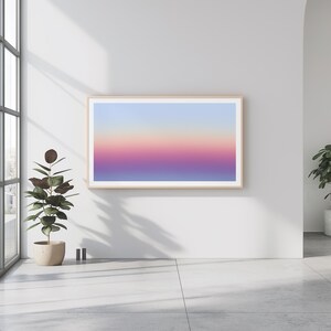 Puede incluir: Una impresión artística enmarcada con un degradado de colores, que va del azul claro en la parte superior al rosa y morado en la inferior. La obra de arte se exhibe en una pared blanca en un entorno interior moderno. Una planta en maceta es visible.