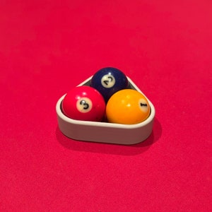 May include: Three billiard balls in a triangle rack. The balls are numbered 1, 2, and 3. The balls are red, blue, and yellow.