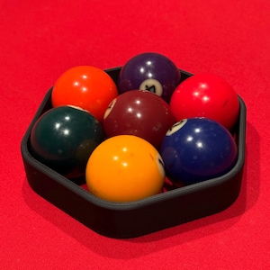 May include: A black hexagonal pool ball rack with seven billiard balls. The balls are red, green, yellow, blue, and maroon.