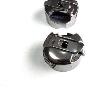 May include: Two silver bobbins for a sewing machine. The bobbins have a metal casing and a small hole in the center.