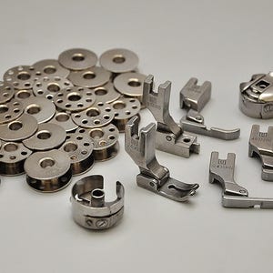 May include: A collection of silver sewing machine bobbins, bobbin cases, and presser feet. The bobbins are arranged in a circle, with the bobbin cases and presser feet scattered around them.