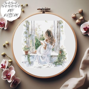 May include: A cross-stitch pattern of a woman sitting by a window, reading a book. The woman is wearing a white dress and has long brown hair. The window is open and there are green plants outside. The pattern is in a white hoop.