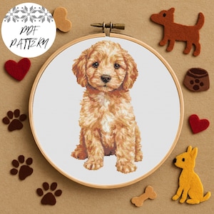 May include: A cross-stitch pattern of a golden puppy in a wooden embroidery hoop. The image is surrounded by felt dog-themed embellishments, including paw prints, hearts, and dog shapes. The text "PDF PATTERN" is in a white circle.