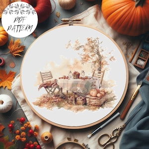 May include: A cross-stitch pattern featuring a table setting with a white tablecloth, a basket of apples, and a tree with fall foliage. The pattern is displayed on a wooden embroidery hoop.