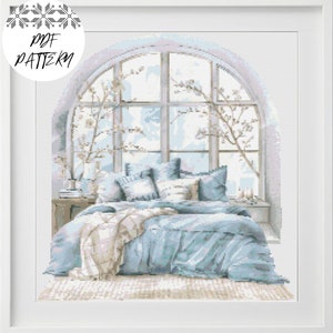 Puede incluir: Una cama azul con almohadas blancas y una manta se encuentra frente a una gran ventana arqueada con moldura blanca. La ventana está decorada con ramas de flores blancas.