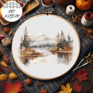 Peut inclure: Un motif de point de croix représentant une peinture à l'aquarelle d'un lac entouré d'arbres et de montagnes. Le lac reflète les arbres et les montagnes. Le motif est dans un cercle de broderie.