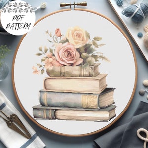 Puede incluir: Una pila de cuatro libros antiguos con un ramo de rosas rosas y crema en la parte superior. Los libros están dispuestos en tamaño decreciente, con el libro más grande en la parte inferior y el más pequeño en la parte superior. Las rosas están dispuestas en un estilo suelto y natural.