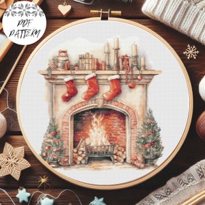 Puede incluir: Un patrón de punto de cruz de una chimenea con calcetines colgados en la repisa, una chimenea encendida y un árbol de Navidad. El patrón está en un aro blanco con las palabras "PDF PATTERN" en la esquina superior izquierda.