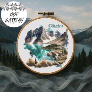 May include: A cross-stitch pattern of a mountain landscape with the word "Glacier" above the mountains. The design is in a wooden embroidery hoop. The words "PDF PATTERN" are in a circle in the upper left corner.