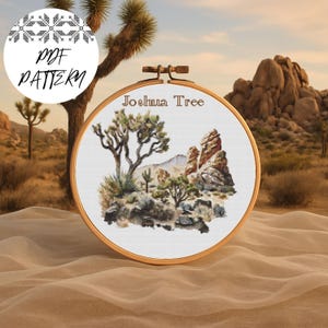 May include: A cross-stitch embroidery hoop depicting a desert scene with Joshua trees and rock formations. The text "Joshua Tree" is stitched above the scene. A circular graphic with the words "PDF PATTERN" is in the upper left.