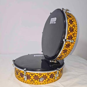 Op de afbeelding: Een paar drums met zwarte vellen en een decoratief geel en bruin sterrenpatroon op de zijkanten. De tekst "POWER BEAT" is zichtbaar op de vellen. De drums staan tegen een witte achtergrond.