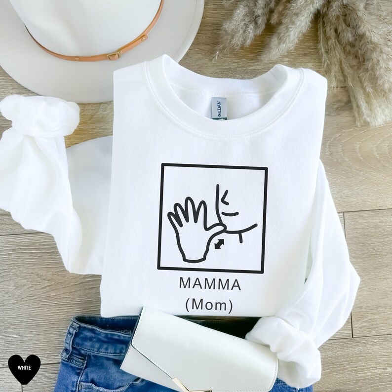 May include: White sweatshirt with a black graphic of a hand signing "mamma" in American Sign Language. The graphic is in a square with the text "MAMMA (Mom)" below it.
