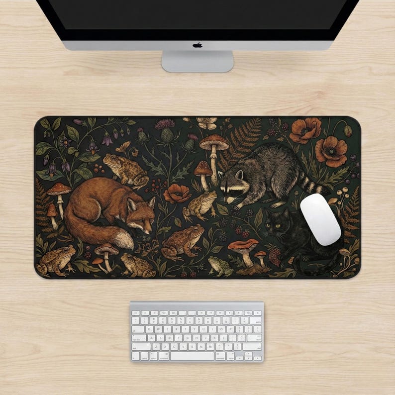 K&ouml;nnte beinhalten: Rechteckige Schreibtischunterlage mit dunkelgr&uuml;nem Design, das einen Fuchs, einen Waschb&auml;ren, eine schwarze Katze, Fr&ouml;sche, Pilze und Blumen zeigt. Detaillierte Illustration von Waldtieren und Pflanzen. Wei&szlig;e Maus und Tastatur sichtbar.