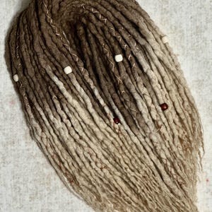 May include: A bundle of handmade dreadlocks in shades of brown and beige, with lighter tips. The dreads are adorned with copper wire accents and small beads. The text "Indoor Lighting" is visible at the bottom of the image.