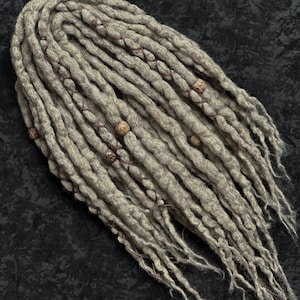 May include: A bundle of light gray dreadlocks with brown accents and decorative wooden beads. The dreadlocks are arranged in a loose, flowing style, with a textured appearance. The beads are spaced along the strands, adding visual interest.