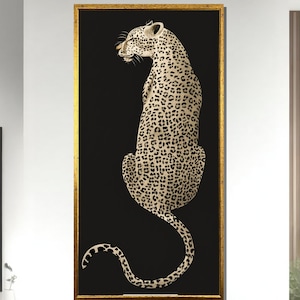 Puede incluir: Una impresión artística enmarcada con una ilustración de un leopardo. El leopardo está representado en posición sentada sobre un fondo negro. El pelaje del leopardo es de color beige claro con manchas marrones oscuras. El marco es dorado.