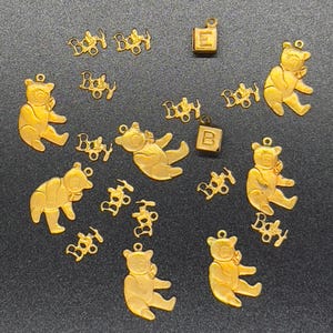 May include: A collection of gold-toned charms featuring baby bears, the word "Baby", and letter blocks. The charms are perfect for adding a personalized touch to jewelry or crafts.
