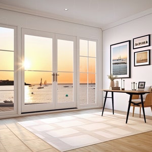 May include: A home office with a desk and chair, a floor lamp, and two potted plants. The room has large windows with a view of a sunset over the ocean with sailboats.