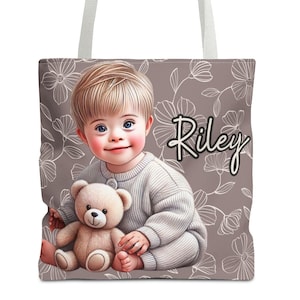 May include: A brown tote bag with a white floral pattern. The bag features a cartoon illustration of a young child with blonde hair holding a teddy bear. The child is wearing a white sweater. The text "Riley" is printed in white on the bag.