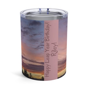 Può includere: Un bicchiere in acciaio inossidabile con un'immagine di tramonto rosa e viola. Il testo "Happy Leap Year Birthday! Riley!" è stampato sul lato del bicchiere.