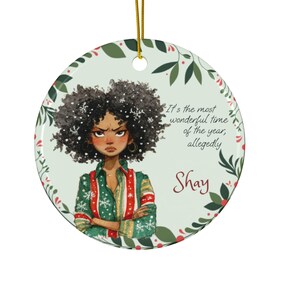 May include: A round Christmas ornament featuring a watercolor illustration of a woman with curly black hair and an angry expression. The ornament has the text "It's the most wonderful time of the year, allegedly" and the name "Shay".