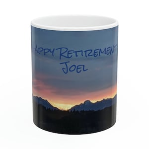 May include: White ceramic mug featuring a sunset mountain scene with the text "Happy Retirement Joel" in blue.