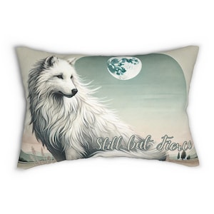 May include: Rectangular pillow featuring a white wolf illustration with the text "Still but Fierce." The artwork includes a full moon and a landscape background in shades of blue, green, and beige. The pillow is designed for decorative use.