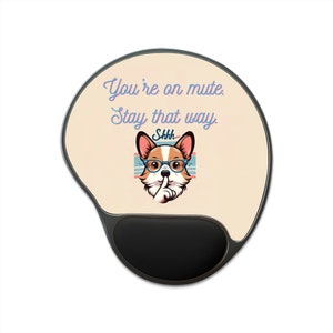 Puede incluir: Alfombrilla de ratón ergonómica con una superficie color crema y un reposamuñecas negro. La alfombrilla presenta un corgi de dibujos animados con gafas y un dedo en los labios, con el texto "You're on mute. Stay that way. Shhh."