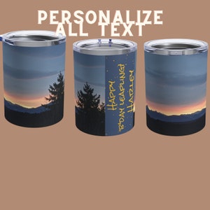 Puede incluir: Tres vasos de acero inoxidable con una escena de montaña al atardecer. El vaso del medio tiene el texto "Happy Birthday Leapling Hartley" en amarillo.
