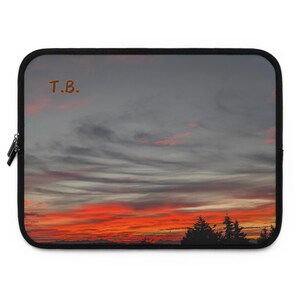 May include: A laptop sleeve with a sunset sky image. The sky is a gradient of orange, red, and pink with gray clouds. The text "T.B." is in the upper left corner of the image.