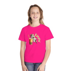 Puede incluir: Una camiseta rosa con un gato de dibujos animados bebiendo t&eacute; de burbujas y la palabra "Kimmy" escrita en una fuente de paja de t&eacute; de burbujas.