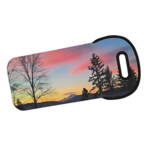 Puede incluir: Un portador de botellas de vino colorido con una escena de puesta de sol con árboles en silueta y un pico de montaña. El portador tiene un asa negra.