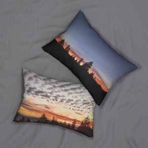 May include: Two decorative throw pillows with sunset scenes. One pillow features a cloudy sunset with a silhouette of trees in the foreground. The other pillow features a blue sky with a silhouette of trees and a sunset in the background.