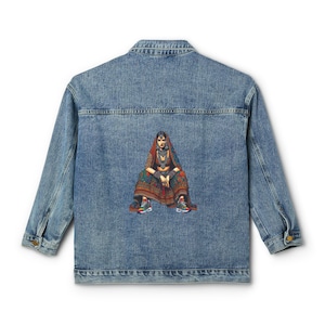 May include: A light blue denim jacket featuring a colorful illustration on the back. The illustration depicts a person in traditional Indian clothing, seated with sneakers. The jacket has a classic collar, button closure, and long sleeves.
