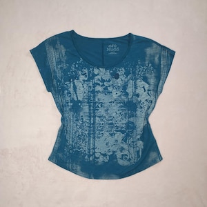 May include: Teal-colored Mudd brand t-shirt with a scoop neck and short sleeves. The shirt features a light blue floral and abstract pattern across the front. The Mudd logo is visible on the upper right chest area.