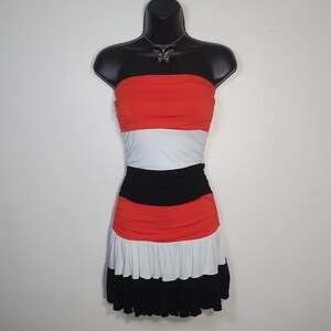 May include: A strapless dress on a black mannequin. The dress features horizontal stripes of red, white, and black. The skirt has a ruffled hemline. A silver butterfly necklace is worn on the mannequin.