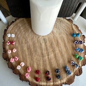 May include: A variety of colorful knotted polymer clay earrings displayed on a wooden surface. The earrings are in shades of red, pink, white, blue, green, and black.
