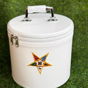 Könnte beinhalten: Runde weiße Aufbewahrungsbox mit Reißverschluss und silbernem Griff. Die Box hat einen gestickten fünfzackigen Stern auf der Vorderseite mit einem bunten Design.