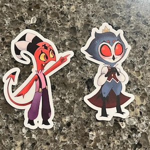 May include: Two cartoon character stickers. One is red with a tail and horns, pointing to the right. The other is blue with a crown and large red eyes.