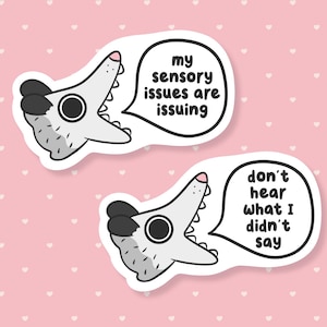May include: Two white stickers with a cartoon alligator design. One sticker has the text "my sensory issues are issuing" in a speech bubble. The other sticker says "don't hear what I didn't say".