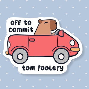 May include: A sticker featuring a cartoon capybara driving a red car. The sticker has the text "off to commit" above the car and "tom foolery" below. The background is light blue with white heart shapes.