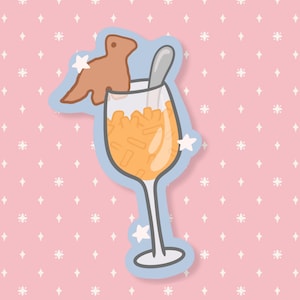 May include: A whimsical sticker featuring a cartoon cocktail in a wine glass, filled with orange liquid and ice. A brown cookie shaped like a creature sits on the rim, with a spoon inside. The sticker has a blue outline and is set against a pink background.