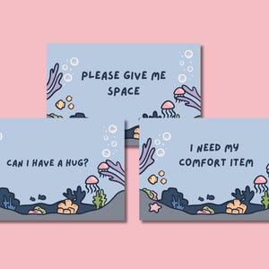 Puede incluir: Tres tarjetas azul claro con un tema submarino. Cada tarjeta tiene un mensaje diferente: "PLEASE GIVE ME SPACE", "CAN I HAVE A HUG?" y "I NEED MY COMFORT ITEM". Las tarjetas presentan ilustraciones de dibujos animados de coral, peces, medusas y burbujas.