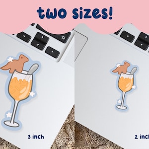 May include: Two stickers on a laptop, featuring a cartoon cocktail with a brown creature and a spoon. The stickers are available in 2-inch and 3-inch sizes. The text "two sizes!" is at the top of the image.