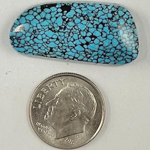 May include: A polished turquoise gemstone with a matrix of black veins. The stone is rectangular with rounded edges. A U.S. dime coin is next to the gemstone for size comparison. The coin is dated 2014.