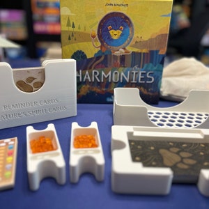 May include: White plastic game components for the board game "Harmonies" by John  Benvenuti. The components include card holders, token trays, and a divider for the game box.