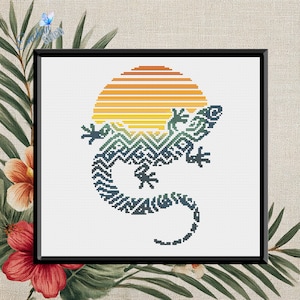 May include: Cross-stitch art featuring a stylized lizard with a geometric pattern in shades of blue and green, set against a yellow and orange sunset. The artwork is framed in black and surrounded by tropical foliage.