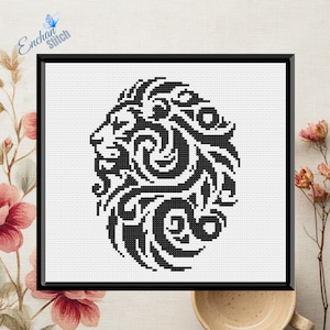 Op de afbeelding: Zwart-wit kruissteekontwerp van een leeuwenkop in een zwarte lijst. De leeuw is in profiel afgebeeld met ingewikkelde, wervelende patronen. De tekst "Enchan Stitch" is zichtbaar. Het kunstwerk staat tegen een witte achtergrond.